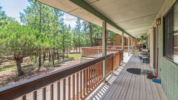 A wooden deck with a railing, a covered area with a view of pine trees, and a building with large windows.