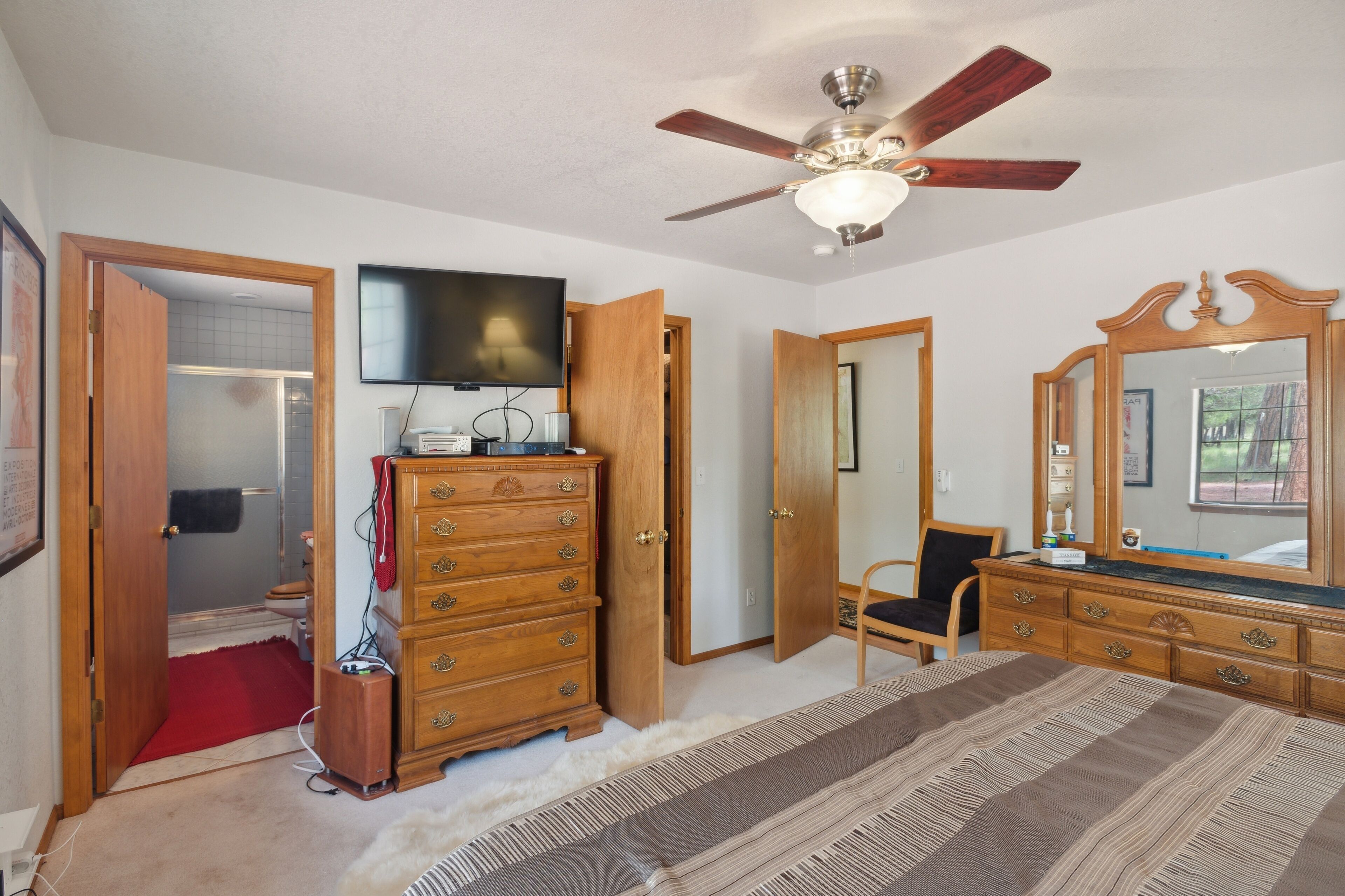 A bedroom with a wooden dresser, a television, a ceiling fan, and a large mirror.