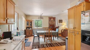 A kitchen with wooden cabinets, a dining table with chairs, a refrigerator, and a window providing natural light.