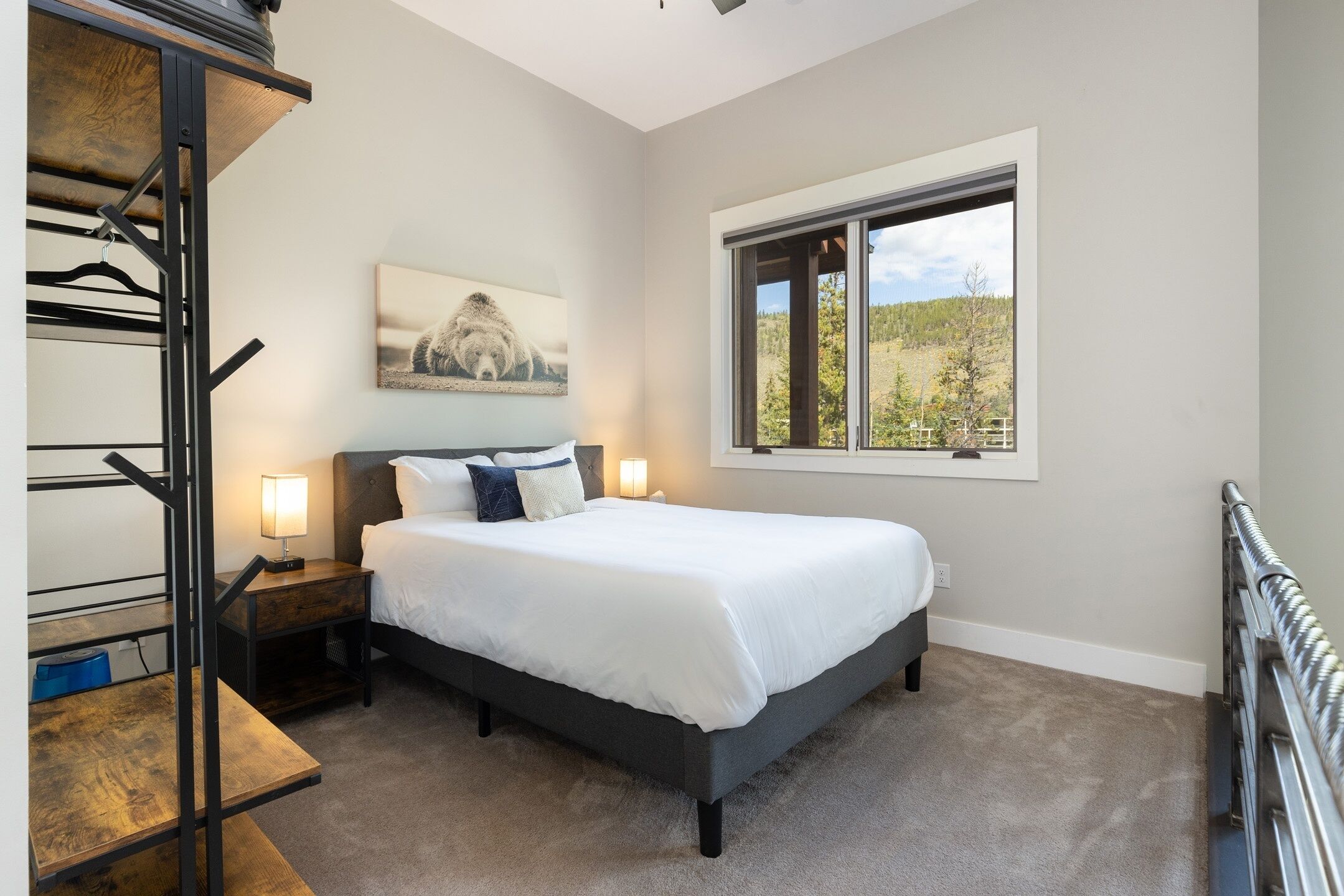 A bedroom with a bed, bedside lamps, a window with a view, a painting on the wall, and a radiator.