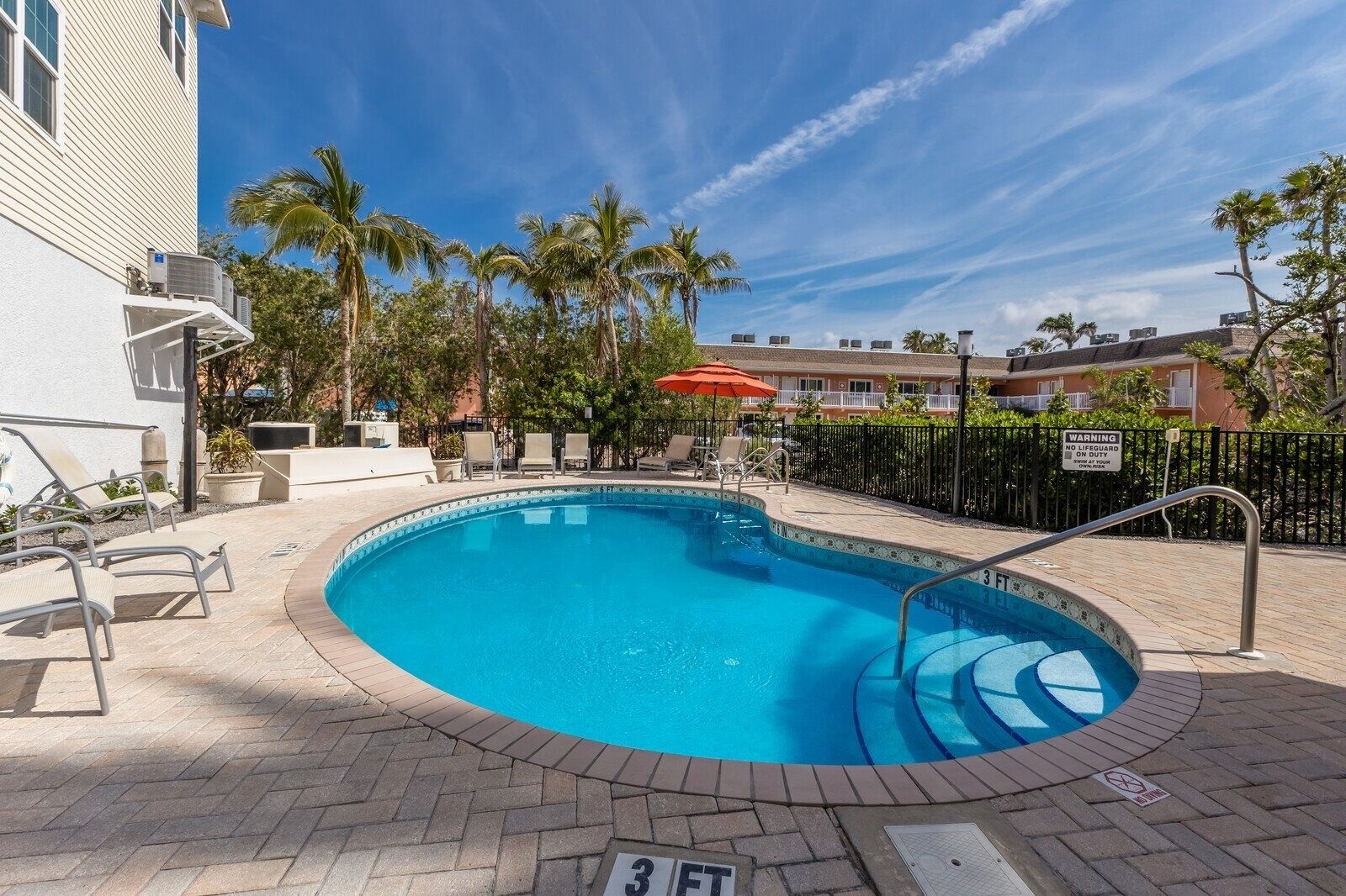 A swimming pool with a 3 FT depth marker, surrounded by lounge chairs and palm trees.