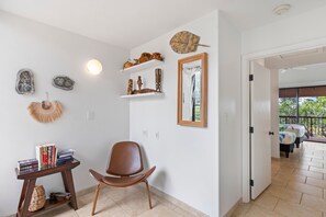 Una habitación con un sillón de cuero marrón, una mesita con libros, decoración en la pared y una puerta que da a un balcón con vistas.