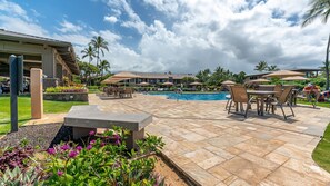 A pool area with lounge chairs and umbrellas, surrounded by a landscaped garden and a building with multiple windows. - Wailea Ekahi, #19a 2 Bedroom Condo by RedAwning (Kihei)