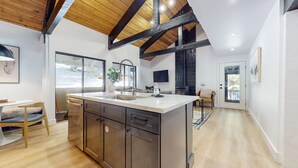 A modern kitchen with a large island, wooden beams, and a view to the outside. - Bigwood #96 2 Bedroom Condo by RedAwning (Mammoth Lakes)