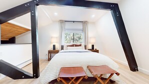 A bedroom with a bed, two bedside tables, a window with curtains, and a view of trees outside. - Bigwood #96 2 Bedroom Condo by RedAwning (Mammoth Lakes)