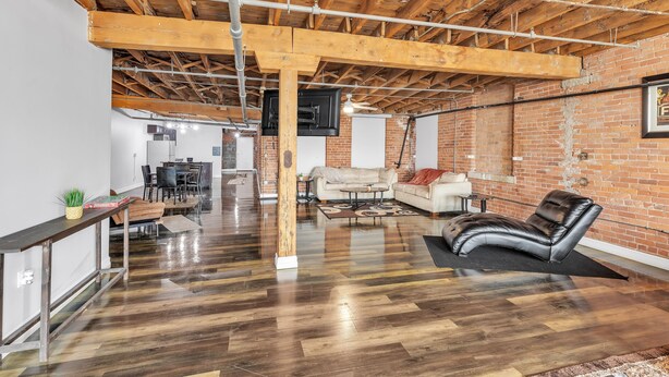 A spacious loft with exposed wooden beams, a polished hardwood floor, a leather sofa, and a brick wall. - Stylish Chic Retreat At Lafayette Lofts 1 Bedroom Apts by RedAwning (Detroit)