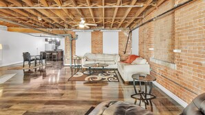 A spacious living area with exposed wooden beams, a brick wall, and a polished wooden floor. - Stylish Chic Retreat At Lafayette Lofts 1 Bedroom Apts by RedAwning (Detroit)