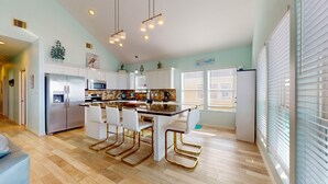 A modern kitchen with white cabinets, a stainless steel refrigerator, a built-in oven, a microwave, and a large island with bar stools.