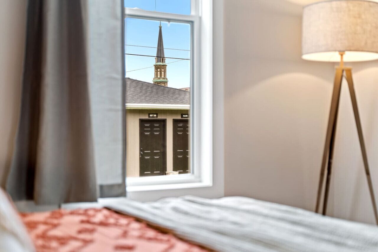 Une chambre d’hôtel avec une fenêtre donnant sur une église et une lampe.
