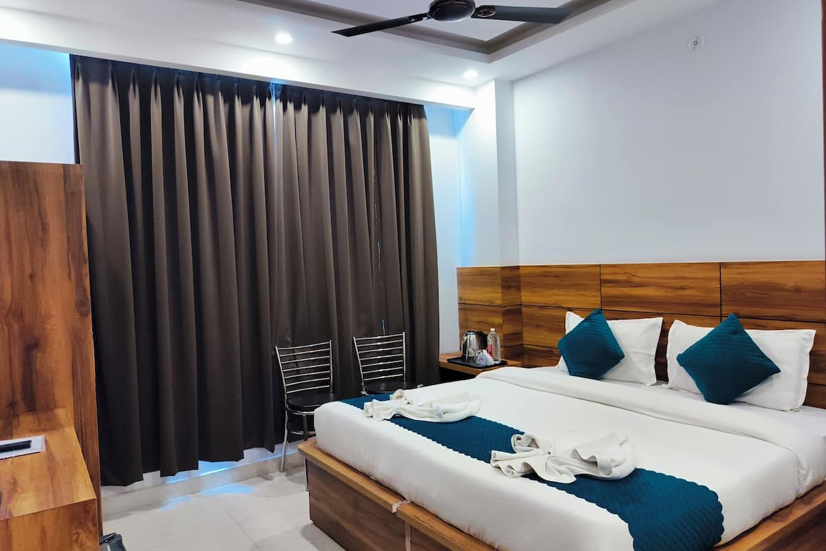 A hotel room with a wooden headboard, a large bed with white and teal bedding, two pillows, a nightstand with a coffee maker, and a ceiling fan.