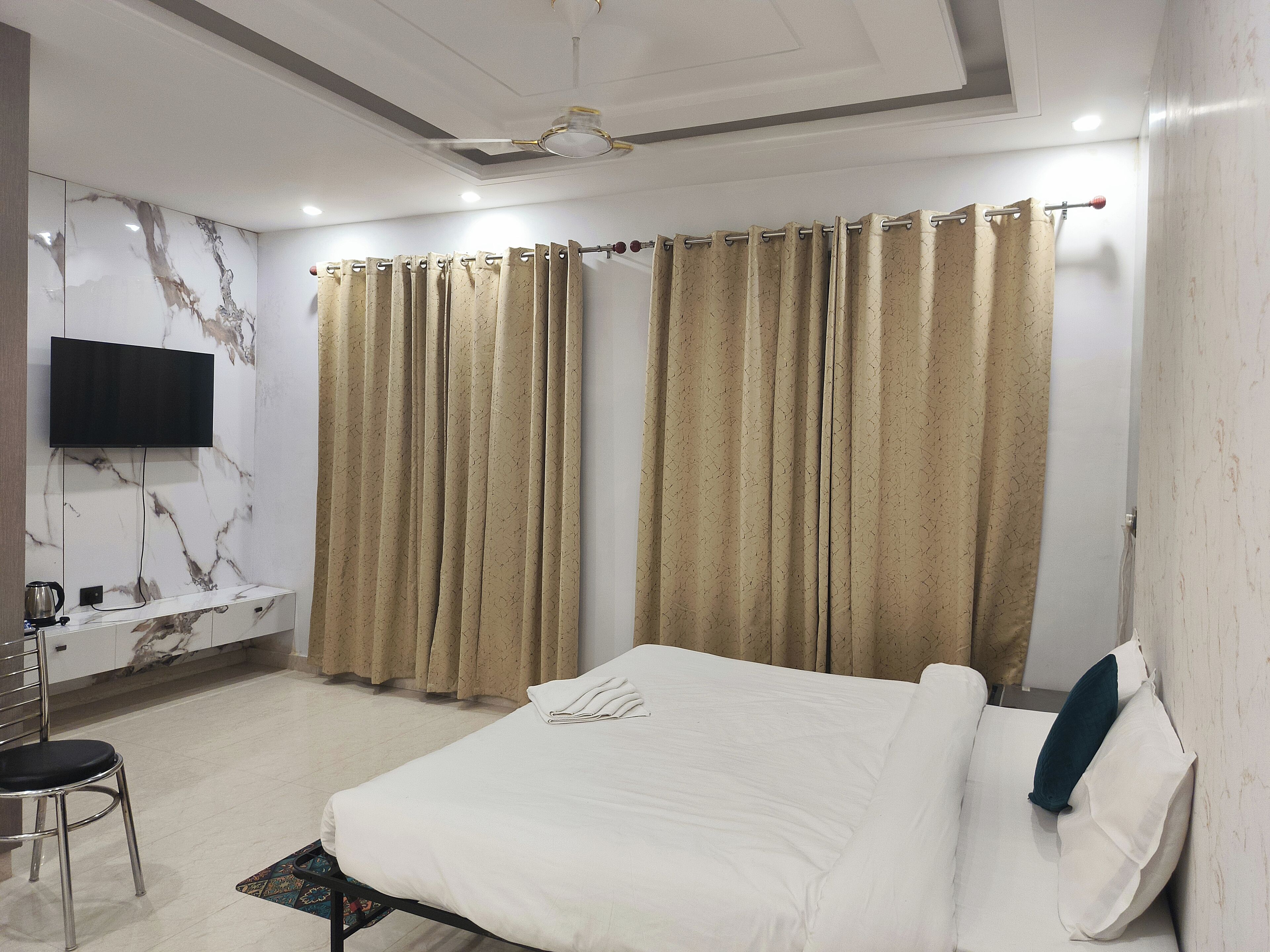 Een hotelkamer met een bed, een aan de muur bevestigde televisie, een bureau met stoel, en gordijnen voor de ramen.