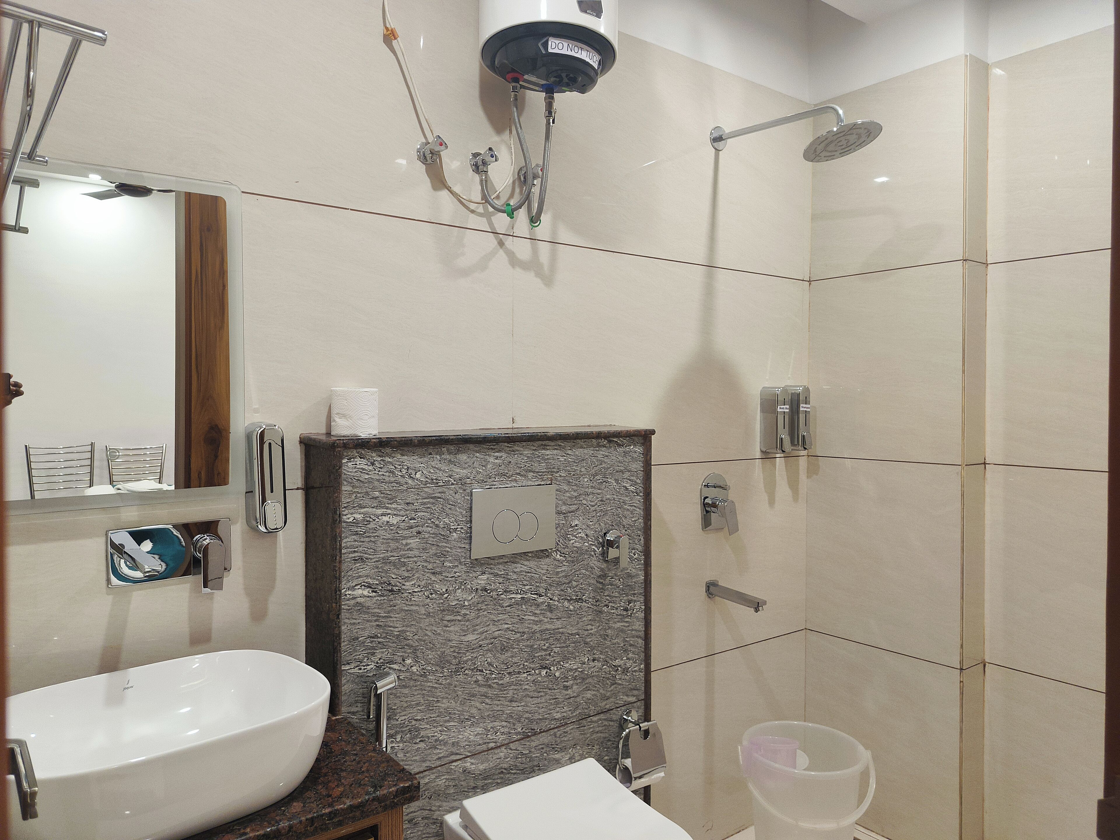 A modern bathroom with a large sink, a mirror, a shower with a handheld showerhead, and a toilet.