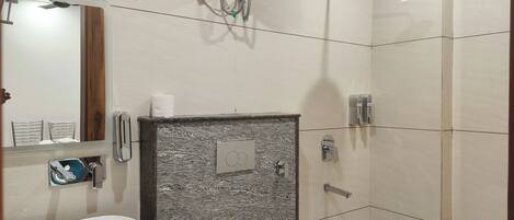A modern bathroom with a large sink, a mirror, a shower with a handheld showerhead, and a toilet.
