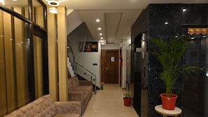 A hotel lobby with a sofa, potted plants, a staircase, and a marble wall. - HOTEL VAIDIK GANGA  (rishikesh)