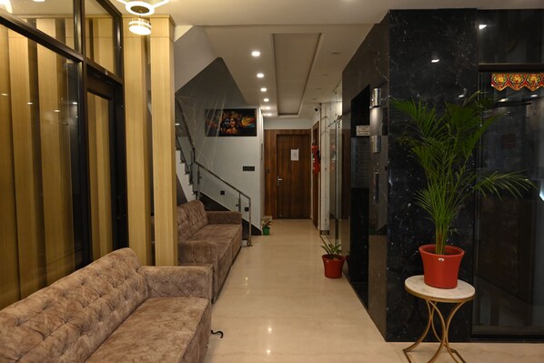 A hotel lobby with a sofa, potted plants, a staircase, and a marble wall. - HOTEL VAIDIK GANGA  (rishikesh)