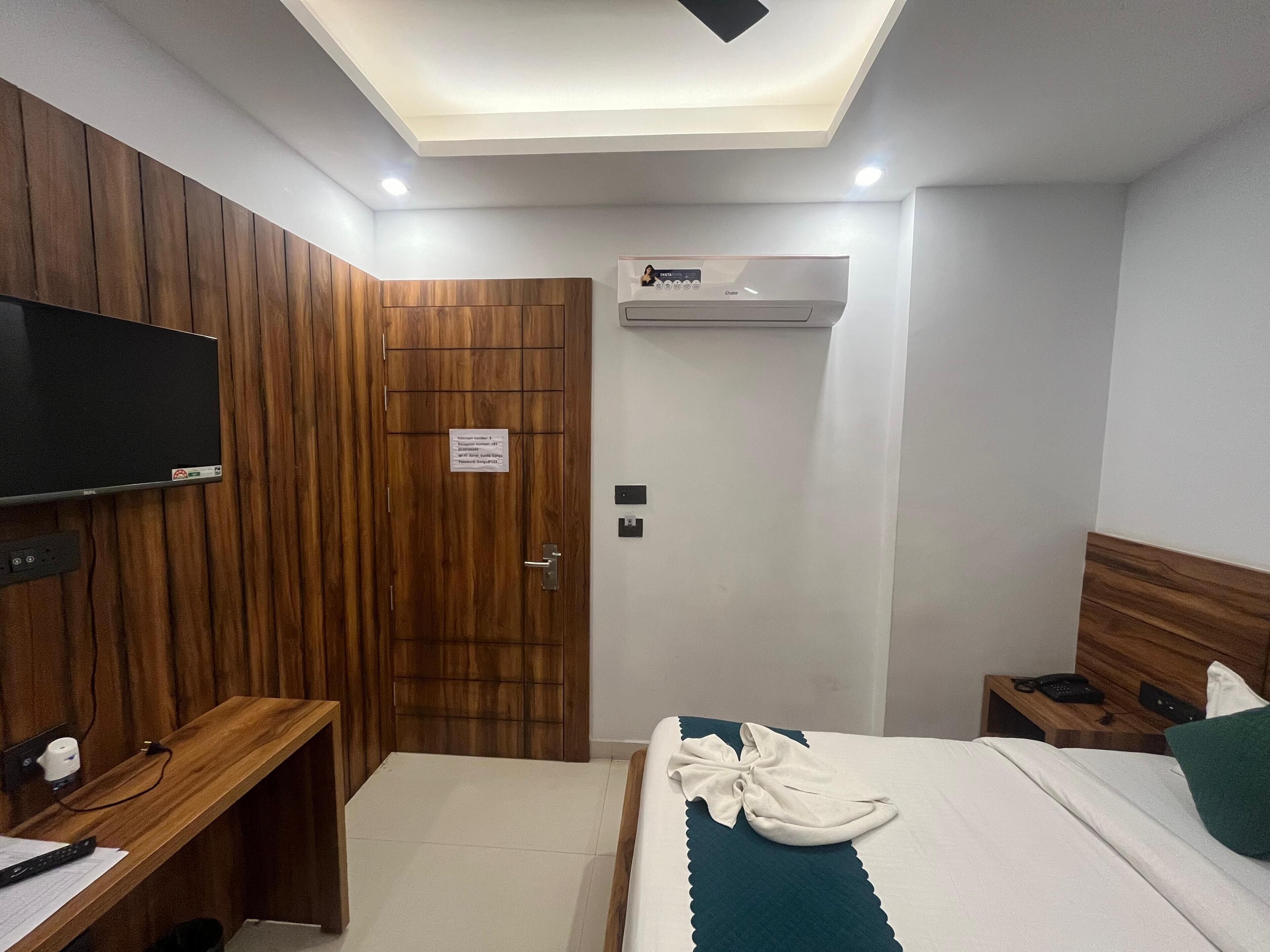 Habitación de hotel con armario de madera, cama con colcha verde, mesita de noche con teléfono y control remoto, y televisor montado.