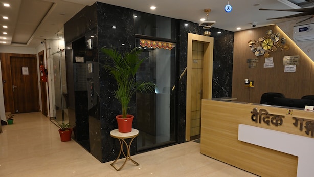 A reception area with a marble wall, a wooden reception desk, and a potted plant. - HOTEL VAIDIK GANGA  (rishikesh)