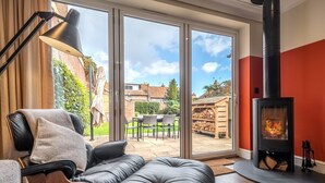 Un salon moderne avec un canapé en cuir, une lampe noire, une cheminée en verre et une vue sur le jardin à travers de grandes portes coulissantes.