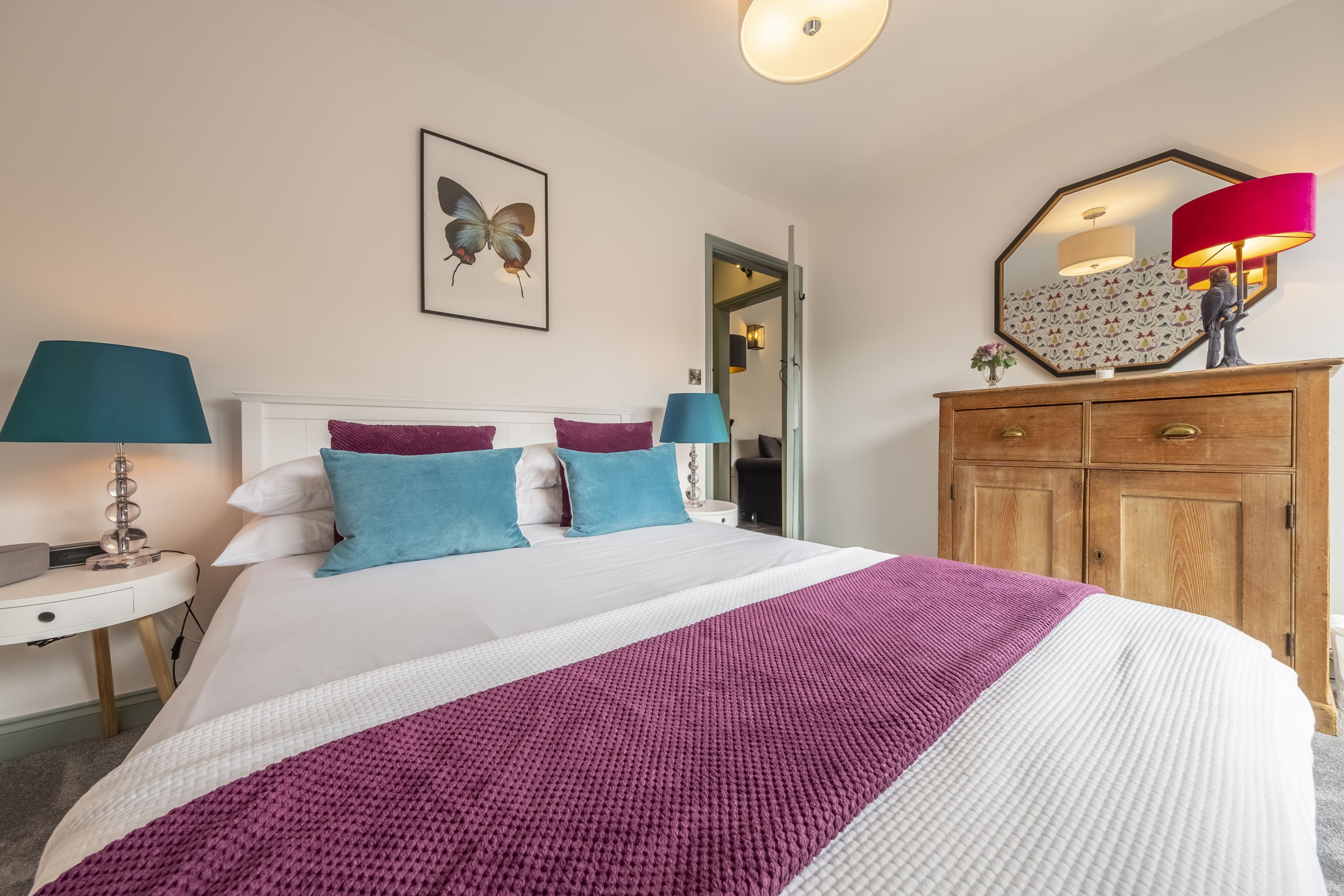 Une chambre à coucher bien rangée, avec un grand lit, deux tables de chevet, une commode en bois et un miroir au-dessus de la commode.