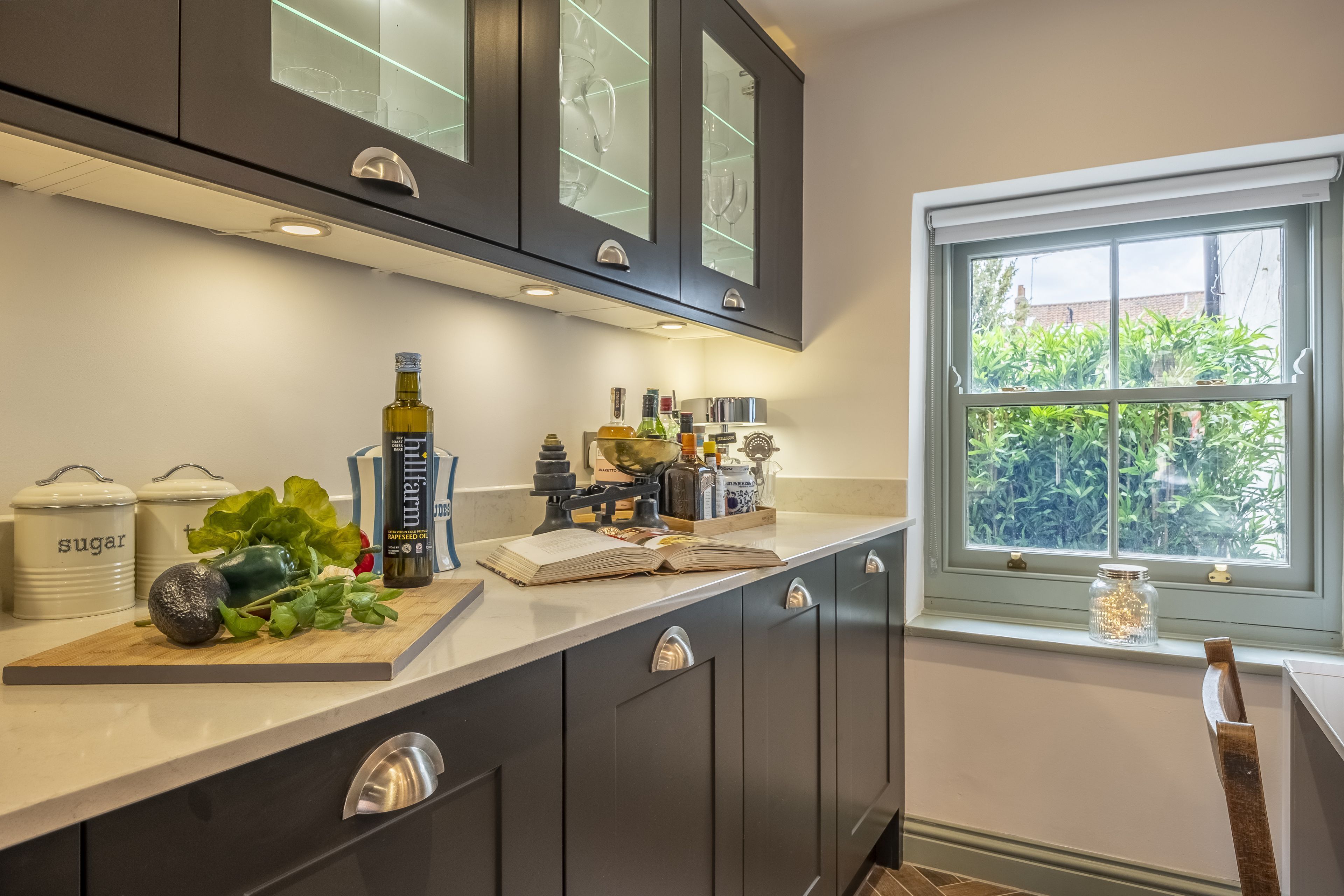 A modern kitchen with dark cabinets, a marble countertop, and a window with a view of greenery.