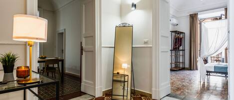 A hotel corridor with patterned flooring, a glass table with a lamp, and a large mirror.