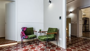 Une pièce avec un sol à carreaux, deux fauteuils verts, une petite table avec une plante et une porte donnant sur une autre pièce.
