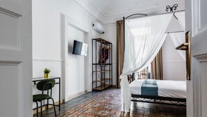 Une chambre à coucher comprenant un lit, un téléviseur fixé au mur, un petit bureau avec une chaise et un motif décoratif sur le sol.