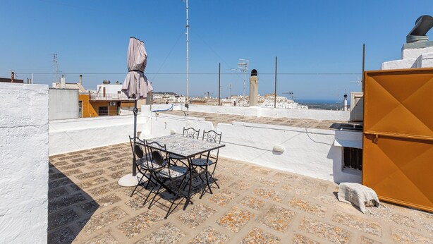 A rooftop terrace with a table and chairs, a covered umbrella, and a view of the cityscape and sea. - 4187 Casa Elen by Barbarhouse (Ostuni)