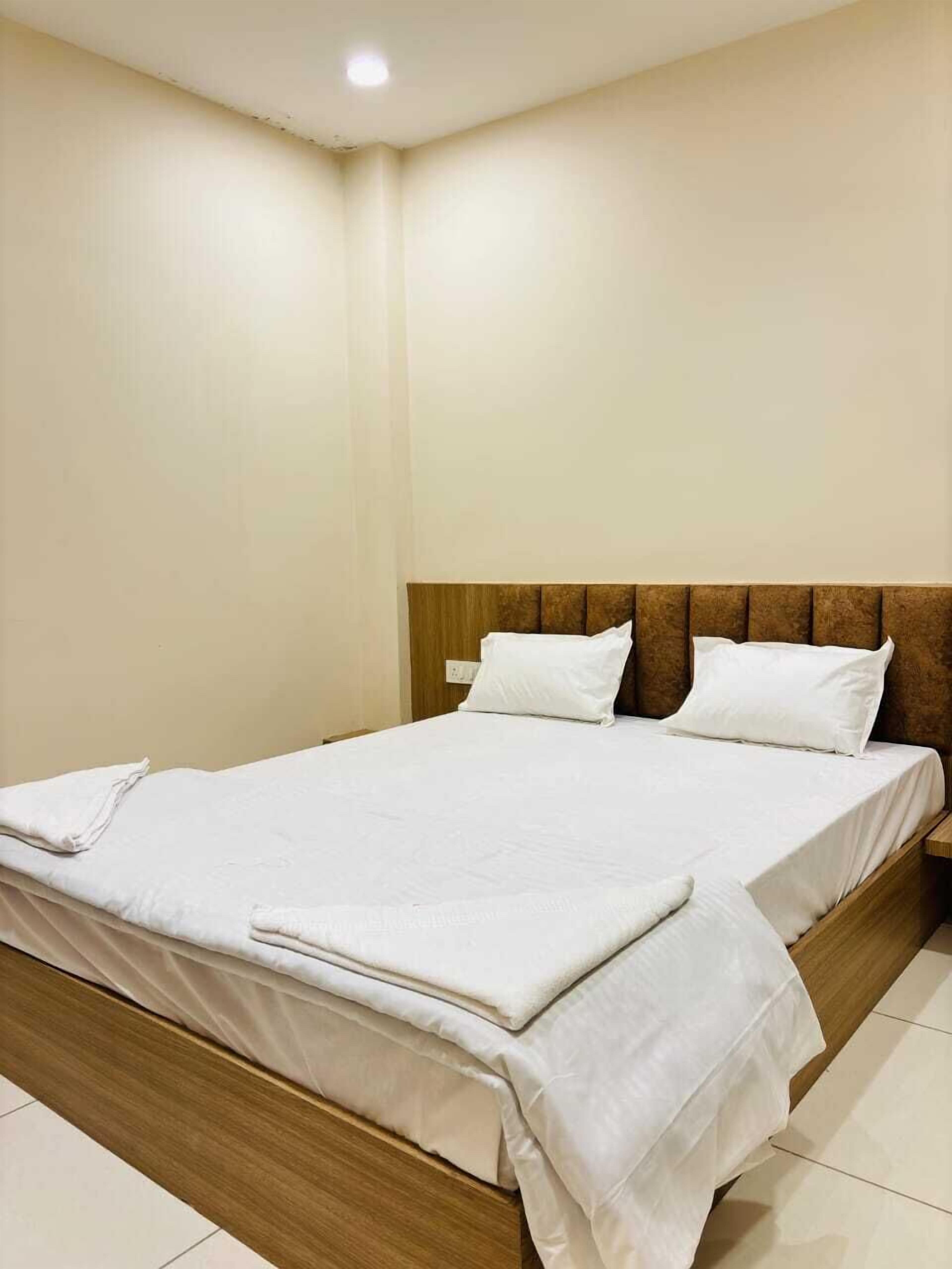 Una cama bien hecha con sábanas blancas en una habitación de paredes lisas y cabecero de madera.