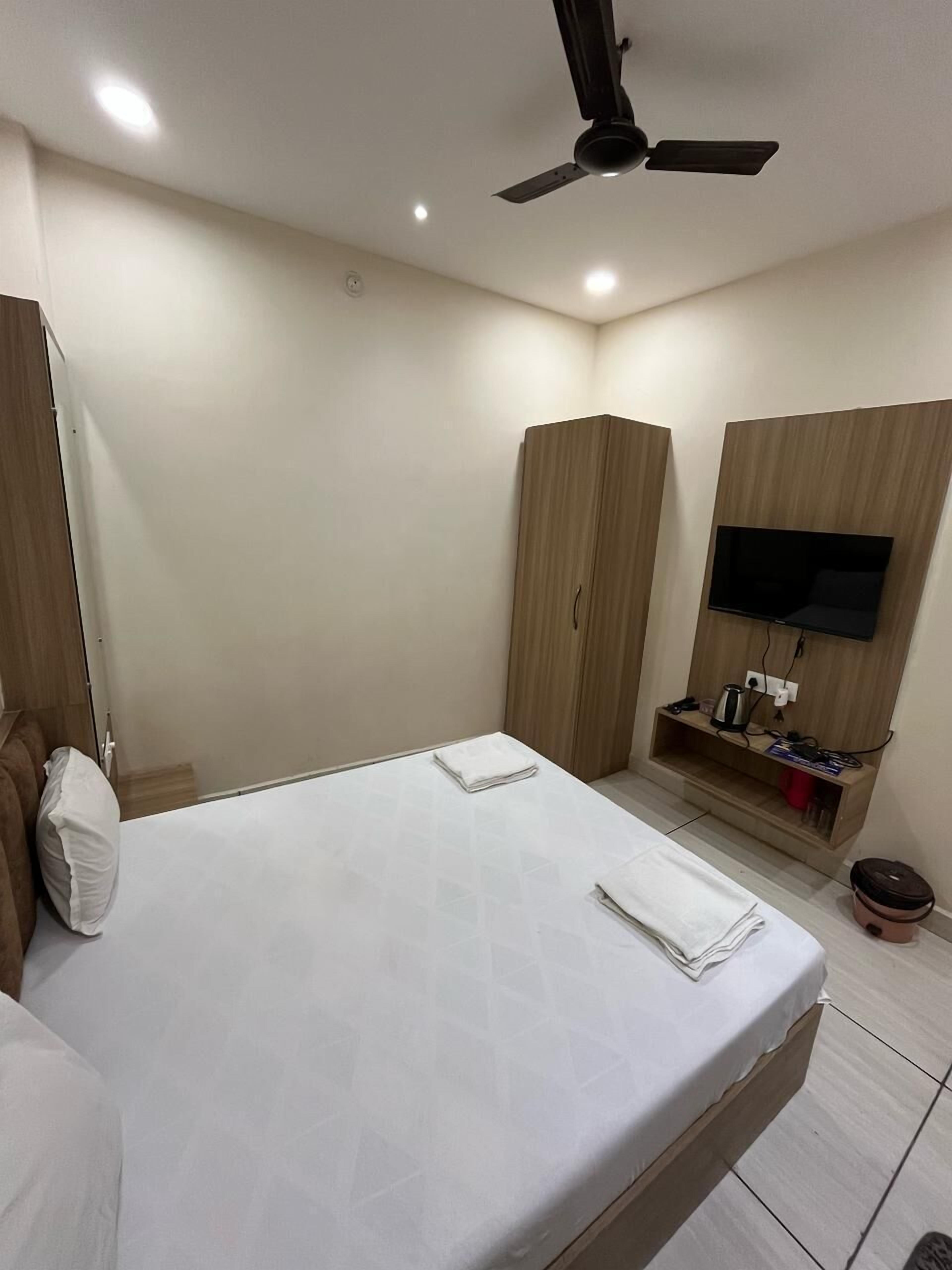 A modern bedroom with a bed, a ceiling fan, a TV mounted on a wooden panel, and a small shelf with items.