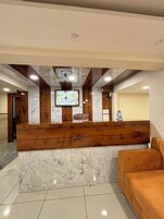 Un área de recepción con mostrador de madera, suelo de mármol y una pantalla de televisión.