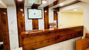 A reception area with a marble counter, wooden accents, and a television screen. - Hotel Shreegopal (Ujjain)
