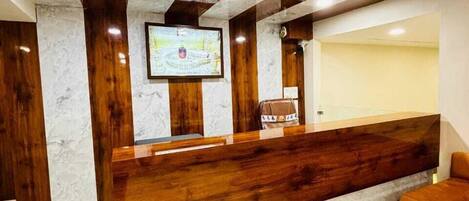 A reception area with a marble counter, wooden accents, and a television screen.
