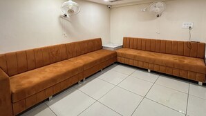 A waiting area with two brown sofas, a marble table, and ceiling fans. - Hotel Shreegopal (Ujjain)