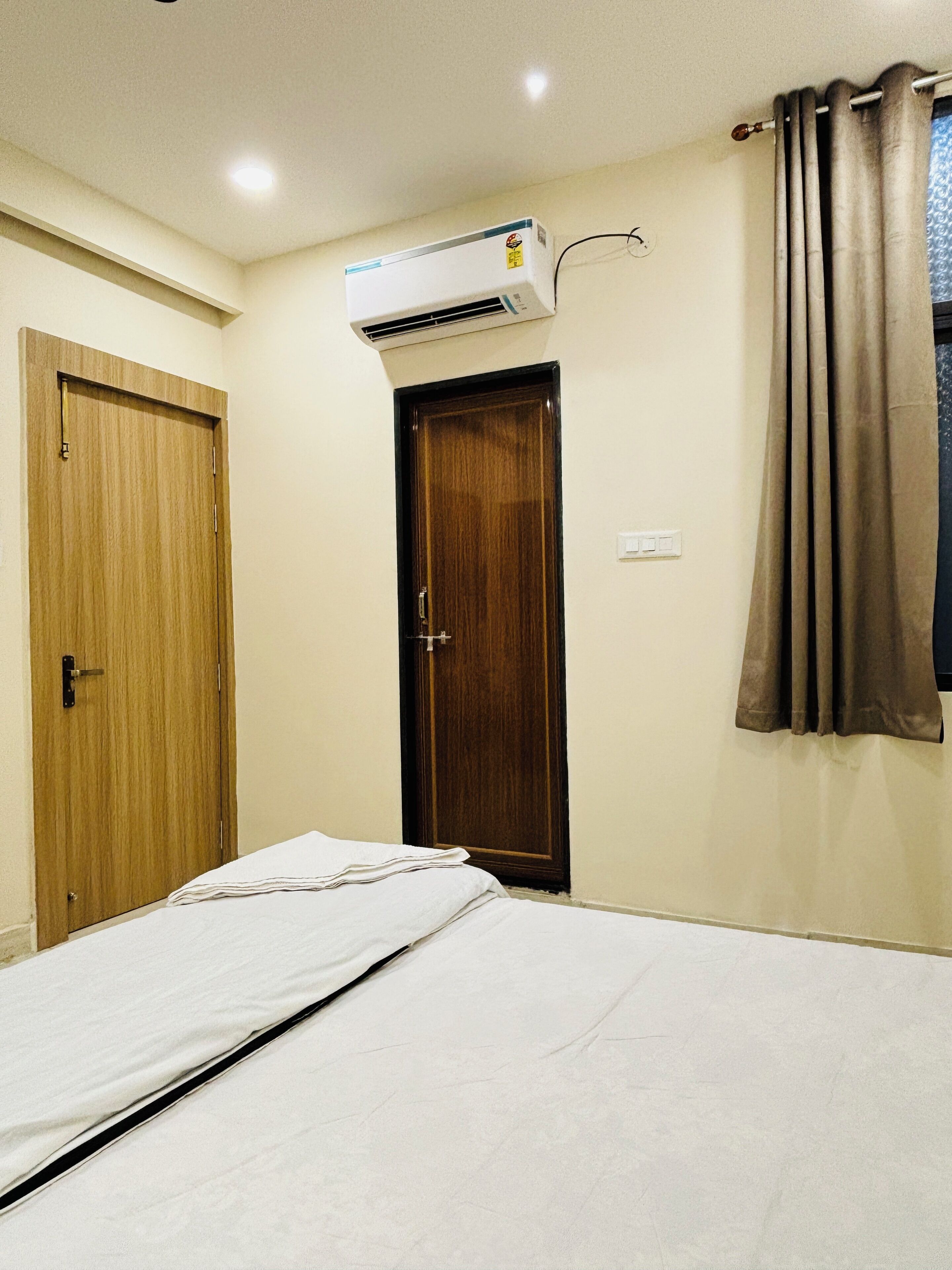 A bedroom with a bed, an air conditioning unit, a wooden door, and a curtain.