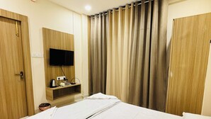 A hotel room with a bed, a ceiling fan, a TV mounted on the wall, and curtains. - Hotel Shreegopal (Ujjain)