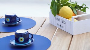 A table with two blue cups and saucers, a white box labeled 'Home & Garden' containing lemons and green leaves.
