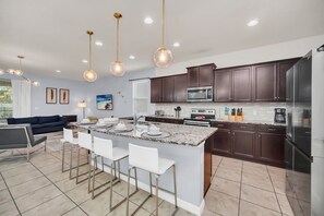 A modern kitchen with dark wood cabinets, a central island with bar stools, and stainless steel appliances. - Star Wars Game Room • Harry Potter Room • Projection Screen • Pool • Near Disney (Kissimmee)