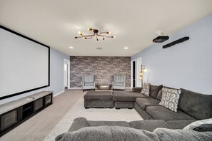 A modern living room with a large screen, comfortable seating, a fireplace, and a projector. - Star Wars Game Room • Harry Potter Room • Projection Screen • Pool • Near Disney (Kissimmee)