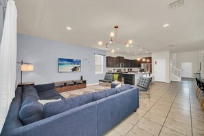A modern living room with a sectional sofa, a dining area with a table and chairs, a kitchen with dark cabinets, and a staircase leading to another level. - Star Wars Game Room • Harry Potter Room • Projection Screen • Pool • Near Disney (Kissimmee)