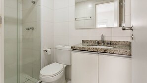 Un baño moderno con cabina de ducha de vidrio, inodoro blanco, lavamanos con encimera de granito y espejo sobre el lavamanos.