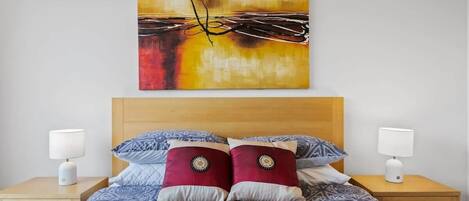 A hotel room with a bed, two bedside tables, and a wall-mounted painting.