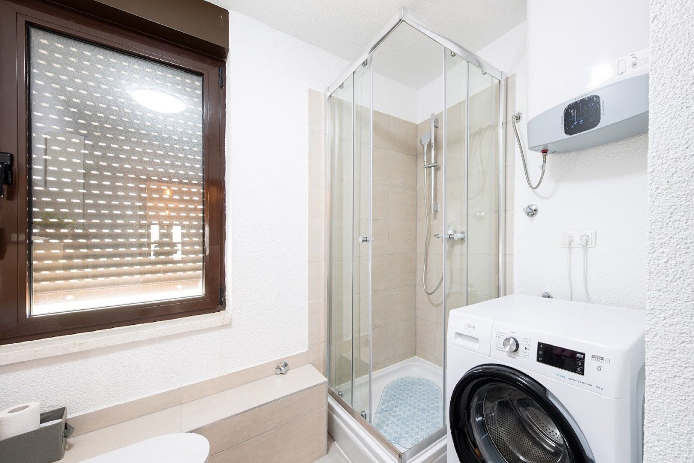 Une salle de bain avec une douche à parois de verre, un lave-linge et des toilettes.