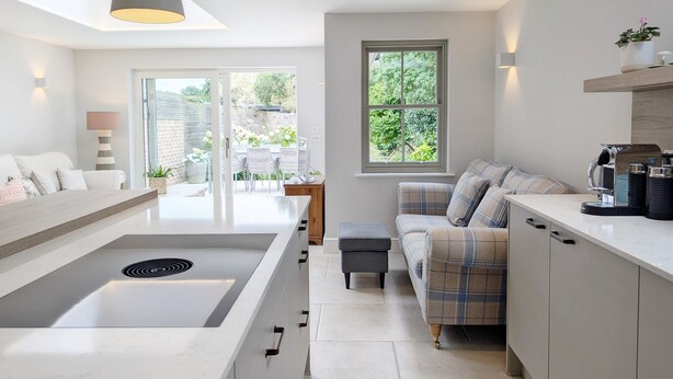 A modern kitchen with a central island, a dining area with a table and chairs, and a seating area with a sofa.