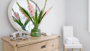 A wooden dresser with a mirror, a vase with pink flowers, and a white chair.
