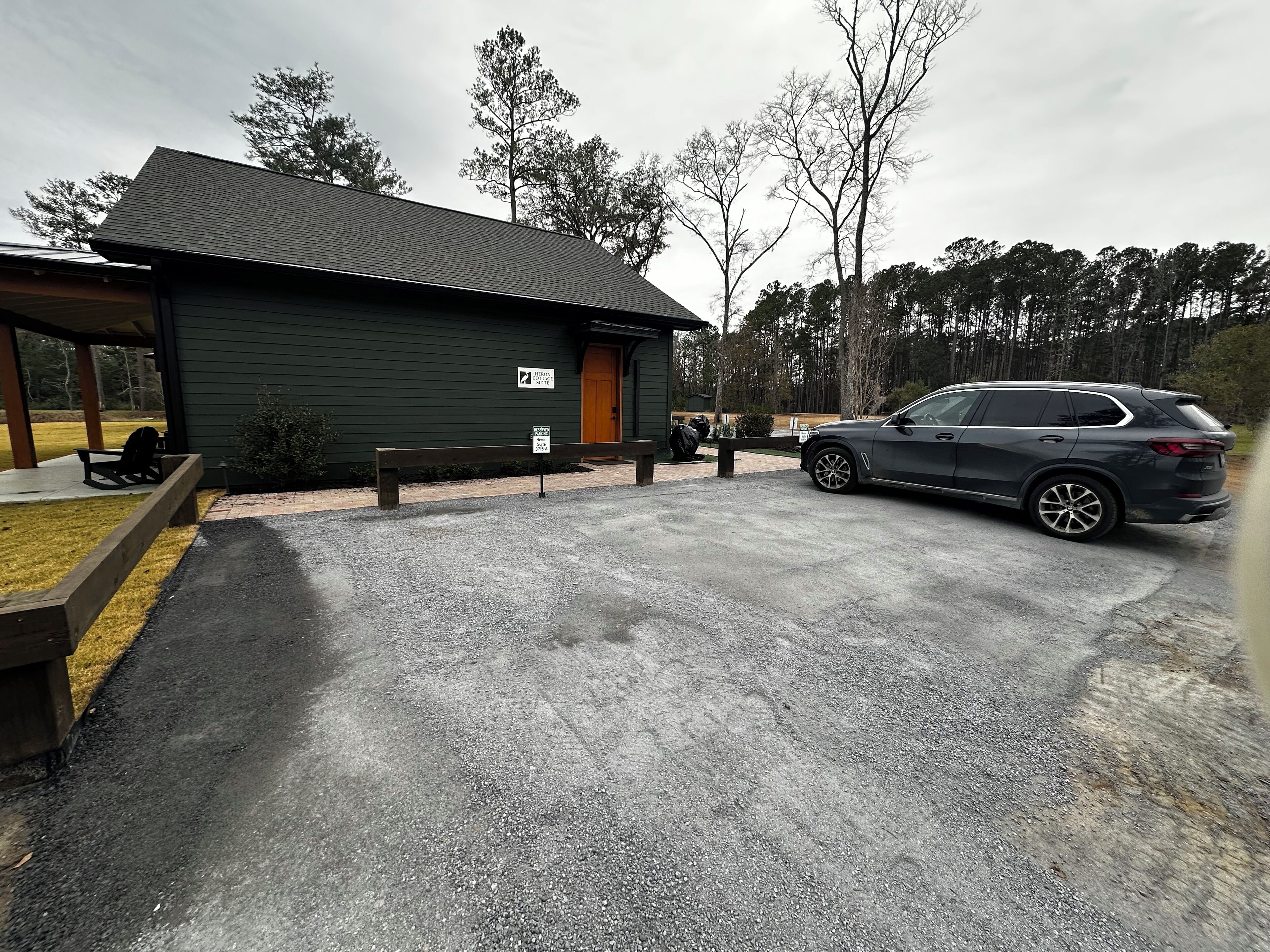 A building with a dark exterior, a wooden bench, and a paved driveway.