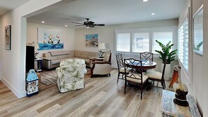 A spacious living room with a high ceiling, a ceiling fan, a dining area with a round table and chairs, a sofa, a coffee table, and a potted plant.