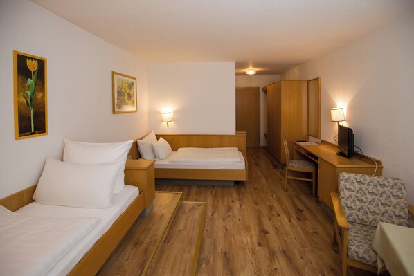 A hotel room with two beds, a desk with a computer, a chair, and a small table. There are wall-mounted lamps and a painting on the wall.