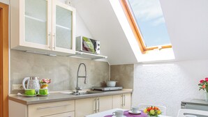 Een kleine keuken met dakraam, witte kastjes en een eethoek met tafel en stoelen.