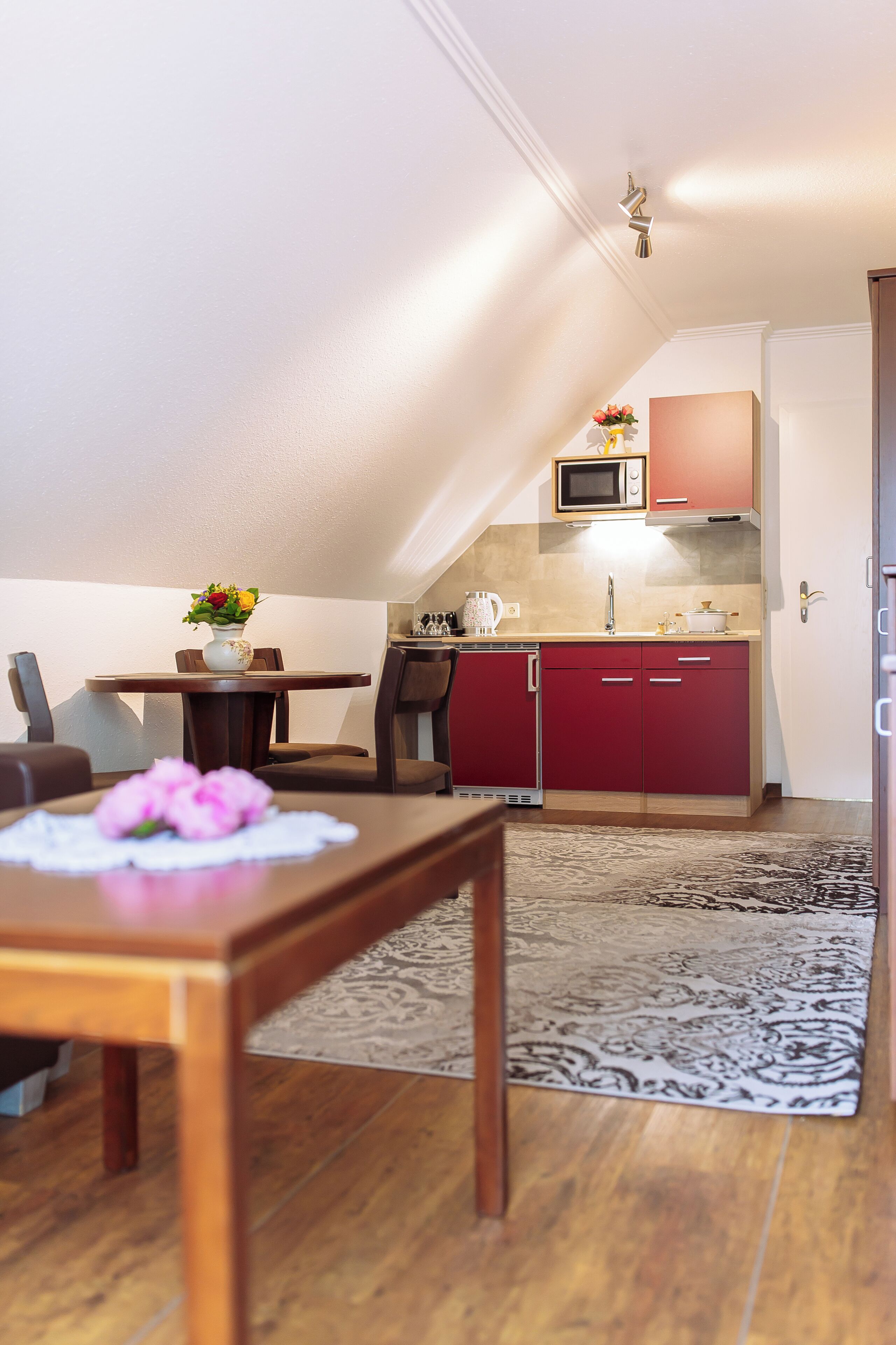 Una cucina compatta con forno a microonde, pensili rossi e una zona pranzo con tavolo e sedie.